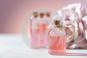 Perfumed Rose Water or essential oil in glass bottle and rose flower on a light background