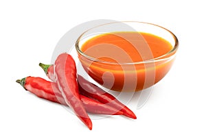 Peri peri chilli sauce in a glass bowl next to three red chillies isolated on white photo