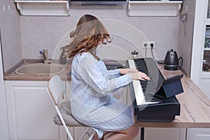 A perky cheerful musician plays the piano while sitting at a musical instrument at home in the kitchen