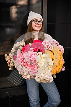 Perky girl in light sweater and jeans stands with a bouquet of colorful flowers photo