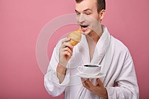 A perky guy in a white bathrobe with croissant
