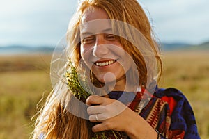 perky laughter on the face of a red-haired girl with freckles who stands in the steppe in an ethnic cape and holds a