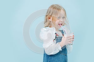 Perky little girl in jeans overalls sipping milkshake through a straw over blue