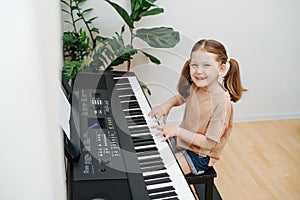 Perky little girl showing off, playing electric piano at home. High angle.