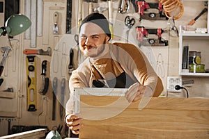 Perky smiling carpenter in a watch cap working in a big workshop