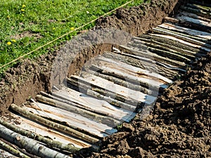 Permaculture trench building with logs of wood with grass side
