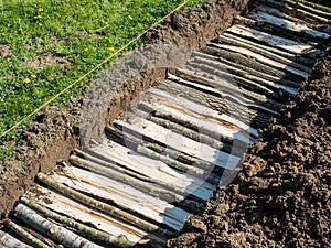 Permaculture trench with logs of wood with green grass side