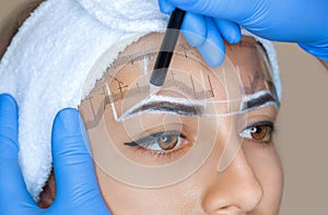 Permanent make-up for eyebrows of beautiful woman with thick brows in beauty salon.