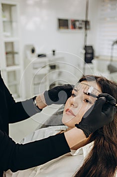 Permanent make-up for eyebrows of beautiful woman with thick brows in beauty salon. Closeup beautician doing tattooing