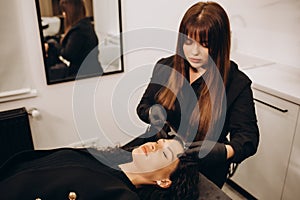 Permanent make-up for eyebrows of beautiful woman with thick brows in beauty salon. Closeup beautician doing tattooing