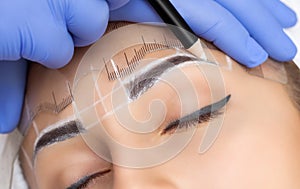 Permanent make-up for eyebrows of beautiful woman with thick brows in beauty salon. photo