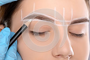 Permanent make-up for eyebrows of beautiful woman with thick brows in beauty salon. Closeup beautician doing tattooing eyebrow.