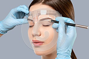 Permanent make-up for eyebrows of beautiful woman with thick brows in beauty salon. Closeup beautician doing tattooing eyebrow. photo