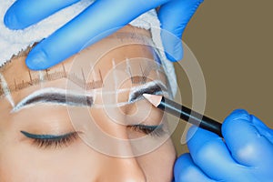 Permanent make-up for eyebrows of beautiful woman with thick brows in beauty salon. Closeup beautician doing tattooing eyebrow.