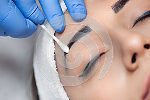 Permanent make-up for eyebrows of beautiful woman with thick brows in beauty salon. Closeup beautician doing  tattooing eyebrow.