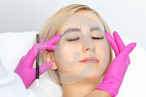 Permanent make-up for eyebrows of beautiful woman with thick brows in beauty salon. Closeup beautician doing tattooing eyebrow.