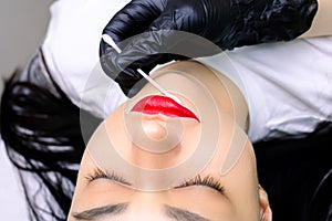 A permanent tattoo master evens out the excess white stroke around the lip with a cotton swab