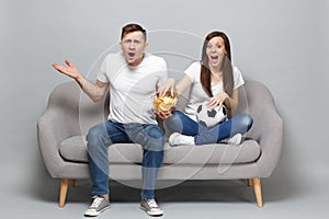 Perplexed couple woman man football fans cheer up support favorite team with soccer ball, hold glass bowl of chips