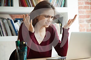 Perplexed female office worker shrugging while looking at laptop