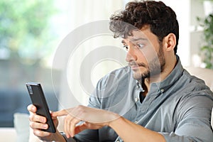 Perplexed man checking cell phone at home