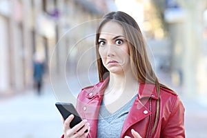 Perplexed woman using phone looks at camera