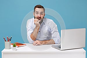 Perplexed young bearded man in shirt sit, work at desk with pc laptop isolated on pastel blue background. Achievement