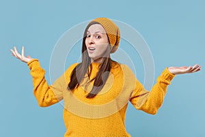 Perplexed young brunette woman girl in yellow sweater and hat posing isolated on blue wall background studio portrait