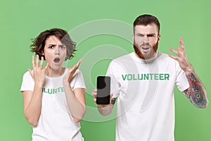 Perplexed young friends couple in white volunteer t-shirt isolated on green background. Voluntary free work assistance