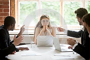 Perplexed young woman looking at coworkers pointing fingers at h photo