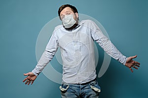 Perplexity man in a medical mask with empty pockets and a questioning look. No money. Concept of economic crisis due to