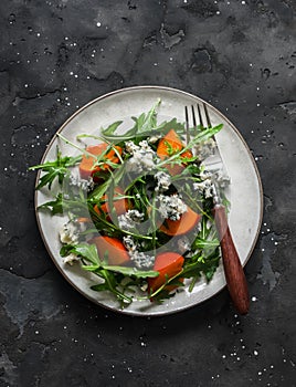 Persimmon, arugula, gorgonzola salad - delicious vegetarian seasonal snack, appetizer on a dark background, top view