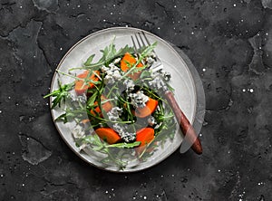 Persimmon, arugula, gorgonzola salad - delicious vegetarian seasonal snack, appetizer on a dark background, top view