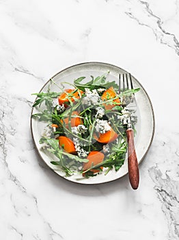 Persimmon, arugula, gorgonzola salad - vegetarian seasonal snack, appetizer on a light background, top view