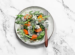 Persimmon, arugula, gorgonzola salad - vegetarian seasonal snack, appetizer on a light background, top view