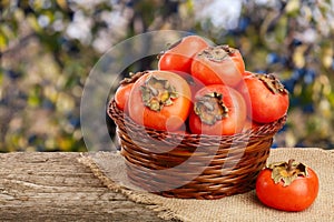 Persimmon fruit in a wicker basket on a wooden table with blurred garden background