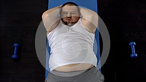 Persistent overweight man doing sit-ups lying on floor, genetic predisposition