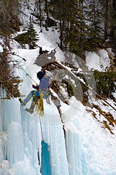 Person abseiling on a large frozen waterfall with huge icicles at Johnston Canyon, Banff