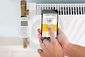 Person Adjusting Temperature Of Thermostat Using Cellphone