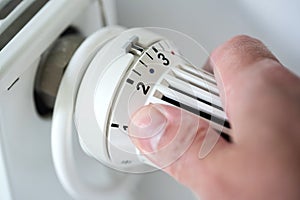 person adjusting thermostat on radiator to lower temperature