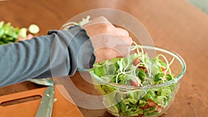 Person assembling leafy green salad with various ingredients in bowl on table