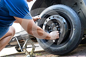 Person attempting to tighten nuts onto temporary car wheel after replacing the flat tire on the street