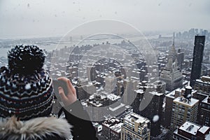 person in beanie taking pictures of snowy cityscape