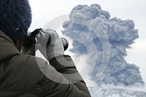 person with binoculars observing ash plume