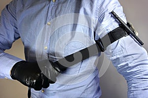 Person in black medical gloves Applies the tourniquet to his hand to prevent bleeding during the first aid. Trauma patient. Combat