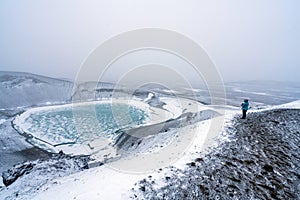 Person with blue jacket ovelooking ice covered Viti volcanic crater near Krafla geothermal area in Iceland.