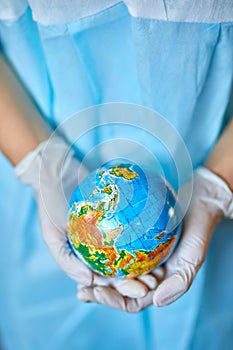 Person in Blue Medical Scrubs Holding a Small Globe Gently in Their Cupped Hands