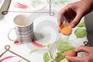 Person breaking an egg shell to separate the yolk from the white.
