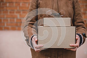 Person in brown coat holding simple paper carboard package