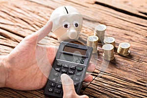 Person Calculating On Calculator With Coins And Piggy Bank