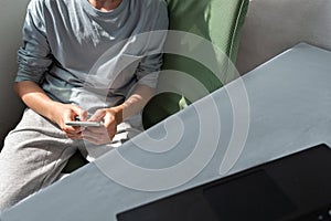 Person in casual clothing sitting at home and holding mobile phone in hands, using social media or messaging, communicating online